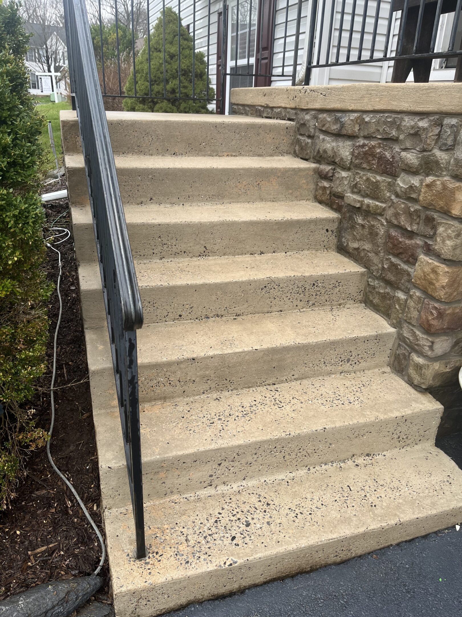 Concrete stairs with a black metal handrail beside a stone wall.