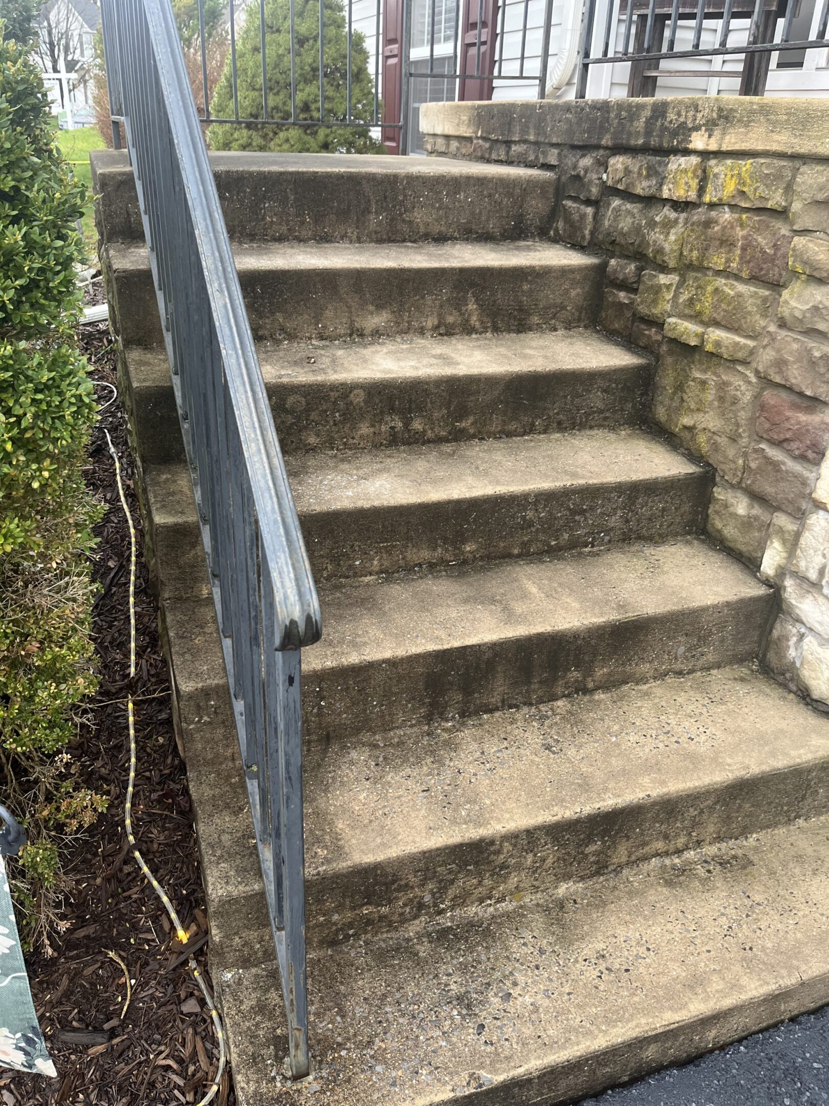 Worn concrete steps with a metal railing beside a stone wall.