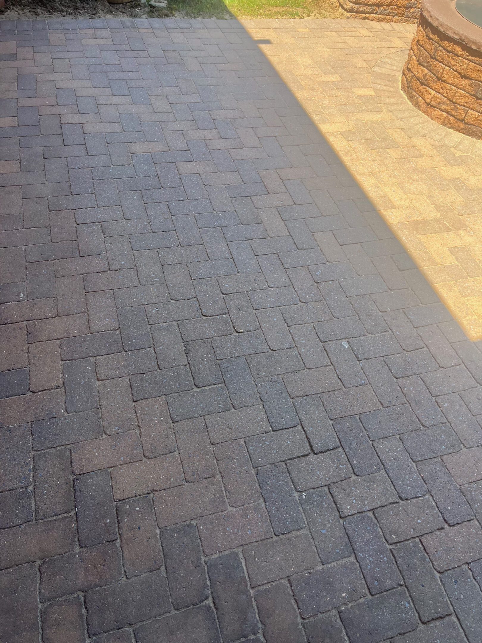 Shadow partially covers a patterned brick pavement under sunlight.