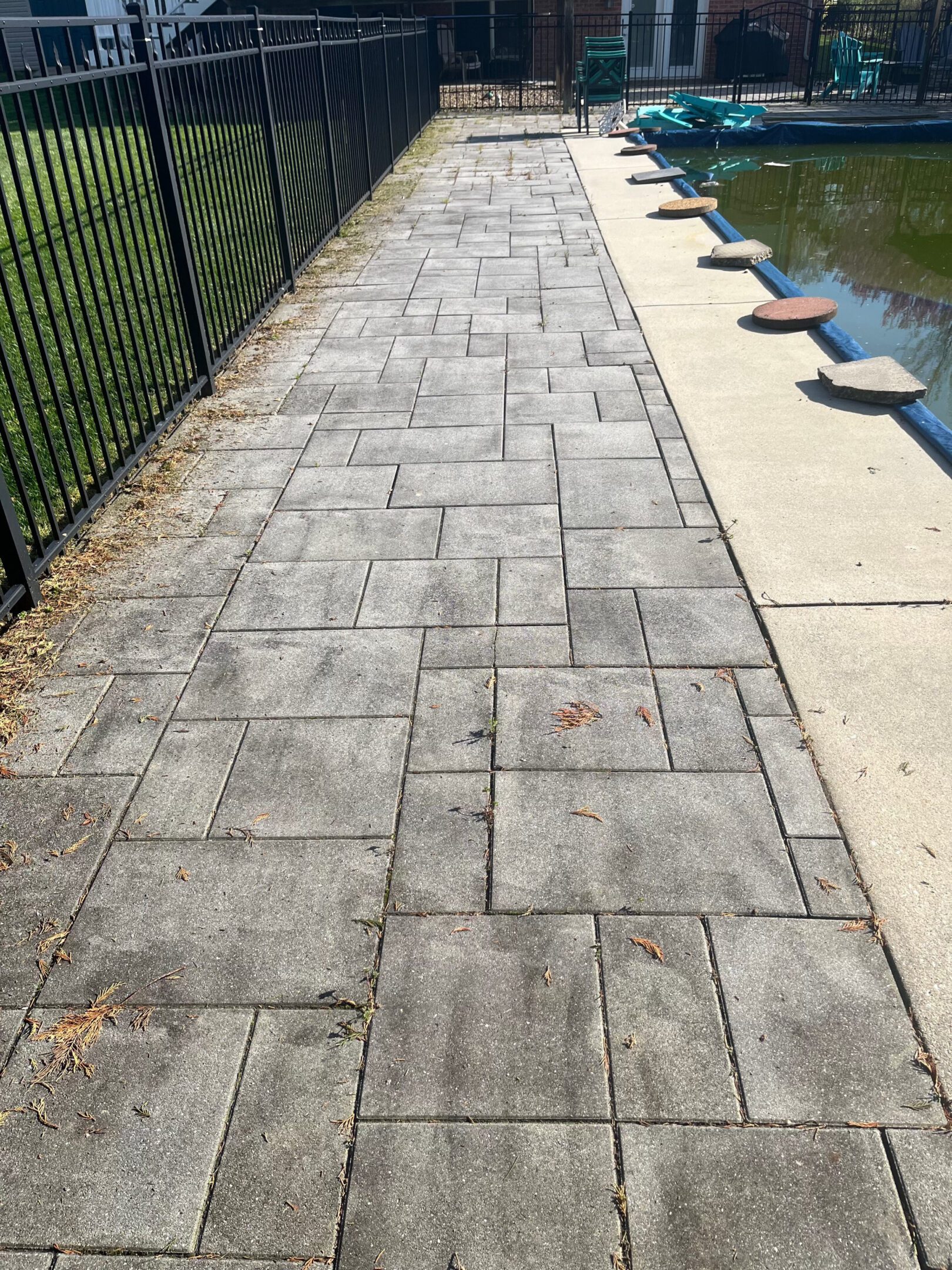 Stamped concrete sidewalk with a fence and adjacent water body.