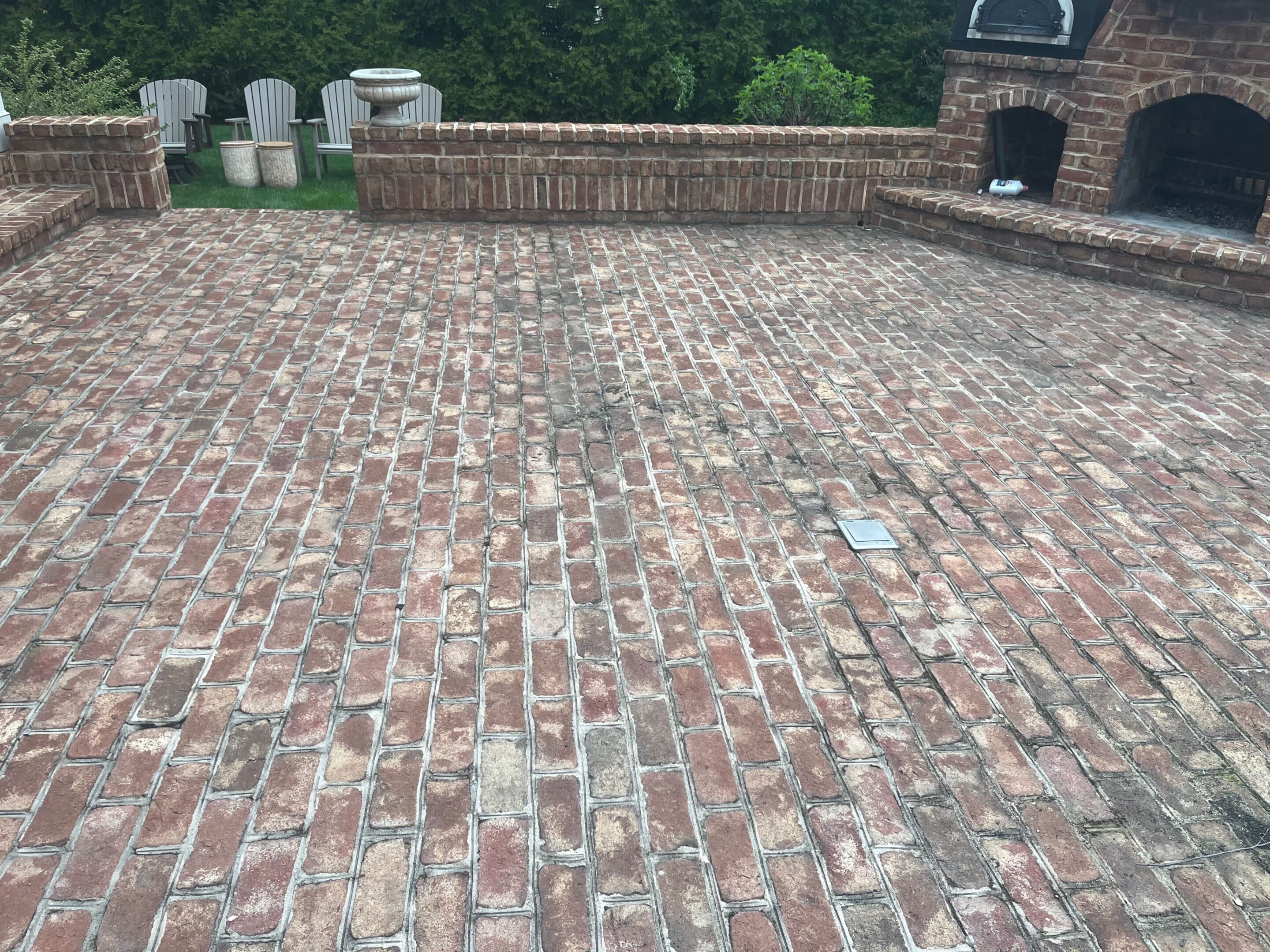 A brick patio with a brick fireplace and white chairs in the background.