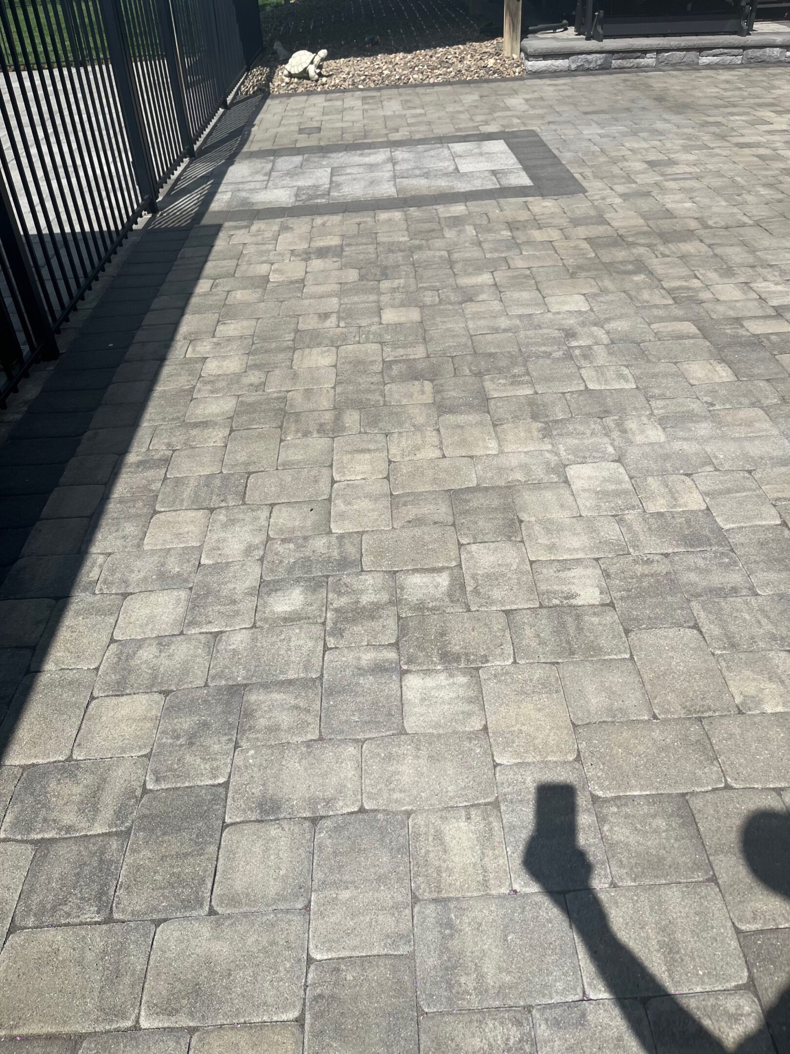 Patterned stone pavement with shadows cast from fence and person.