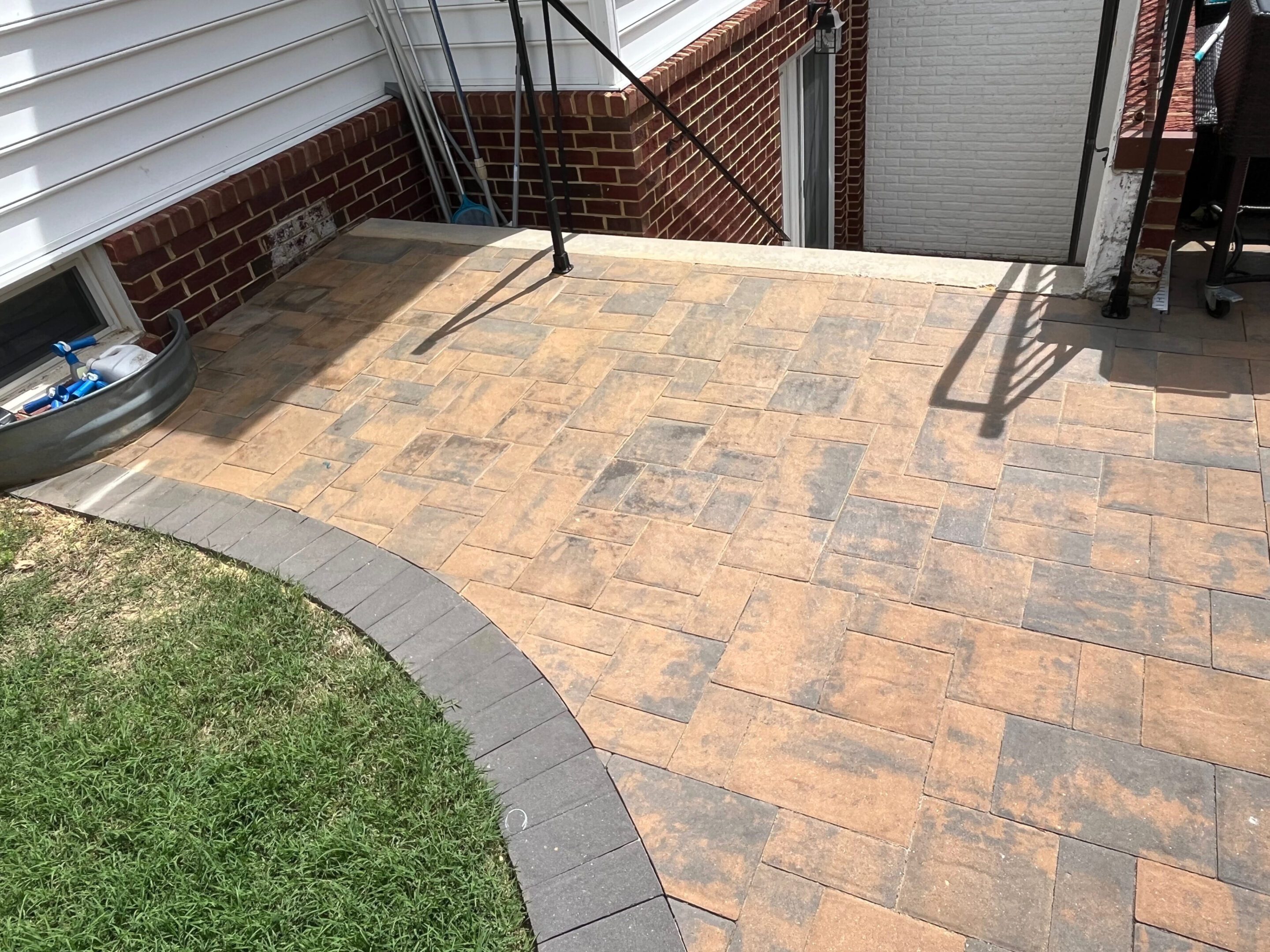Clean, patterned stone patio with a curved border next to green grass.