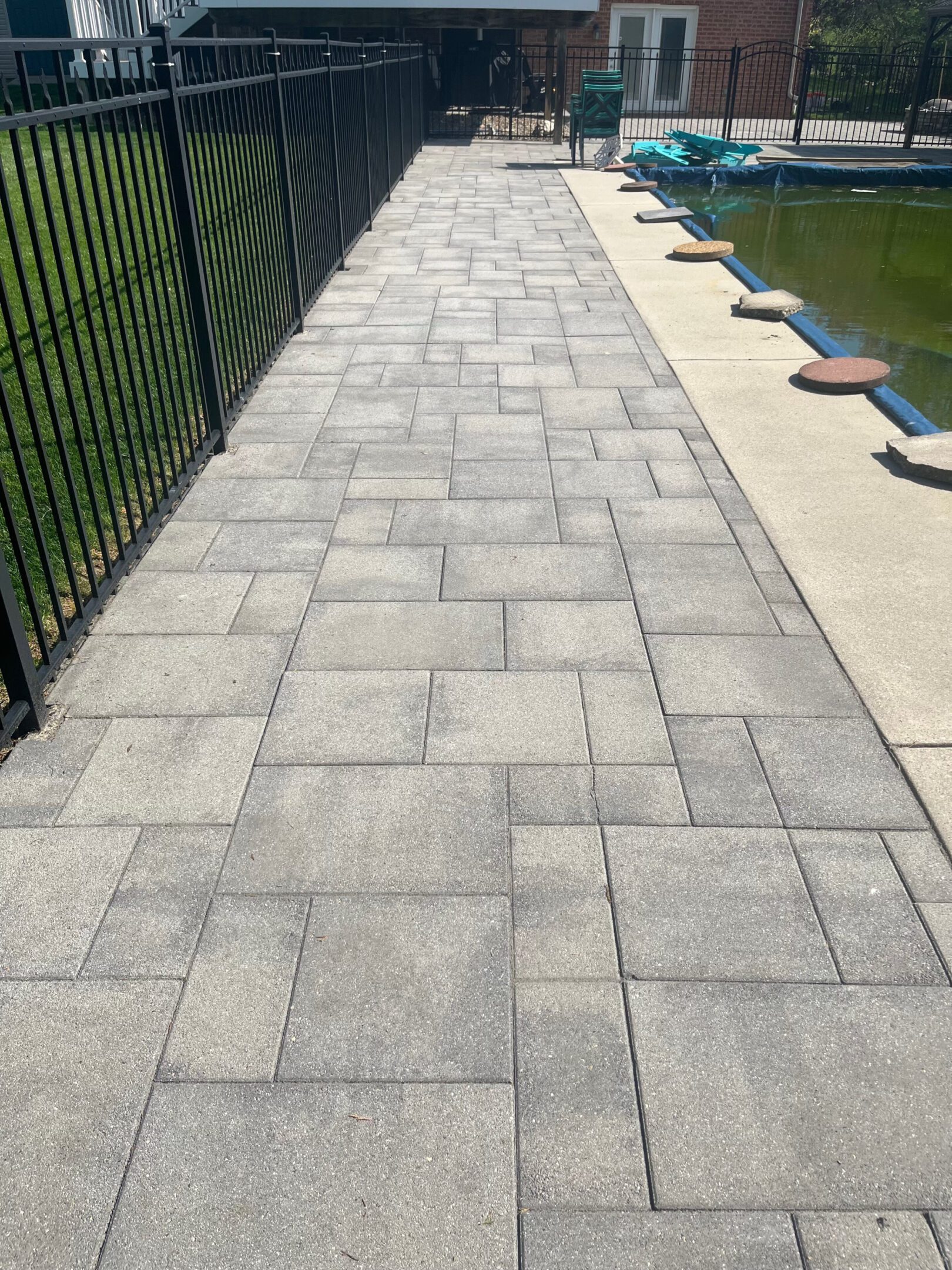 A clean, paved walkway beside a body of water with a black fence on one side.