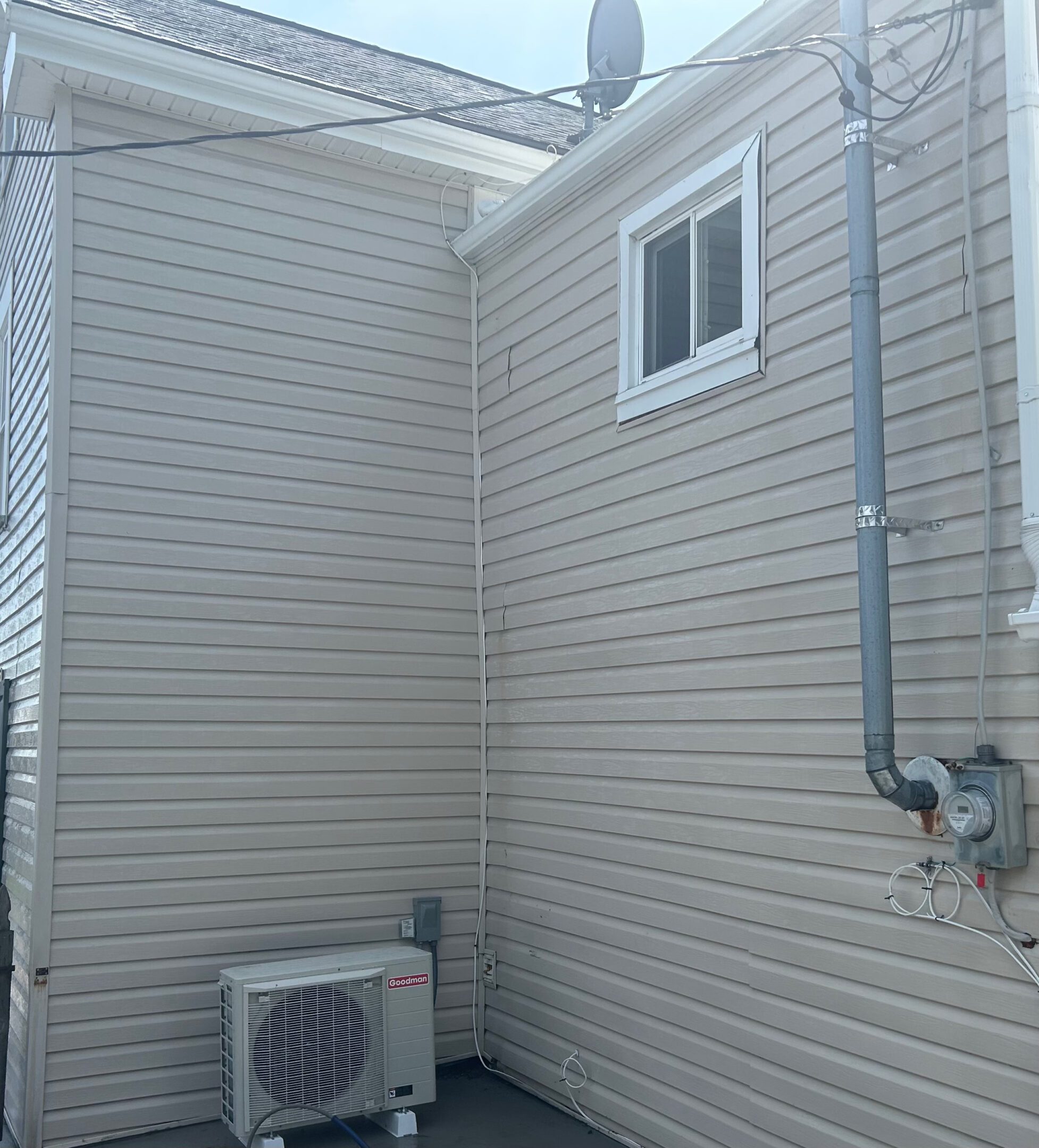 Corner of a building with beige siding and an air conditioning unit.