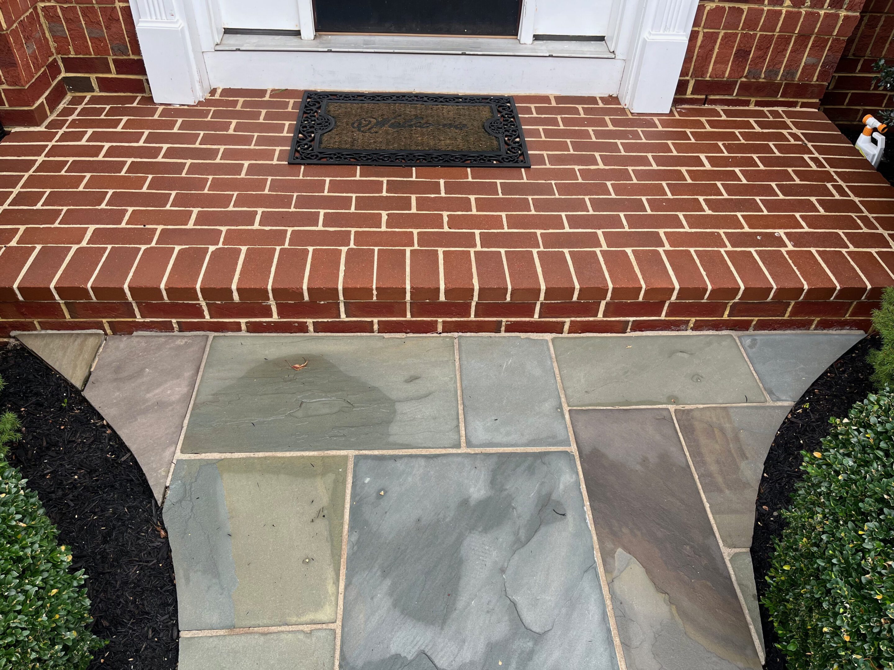 Newly installed stone patio with brick step and doormat at entrance.