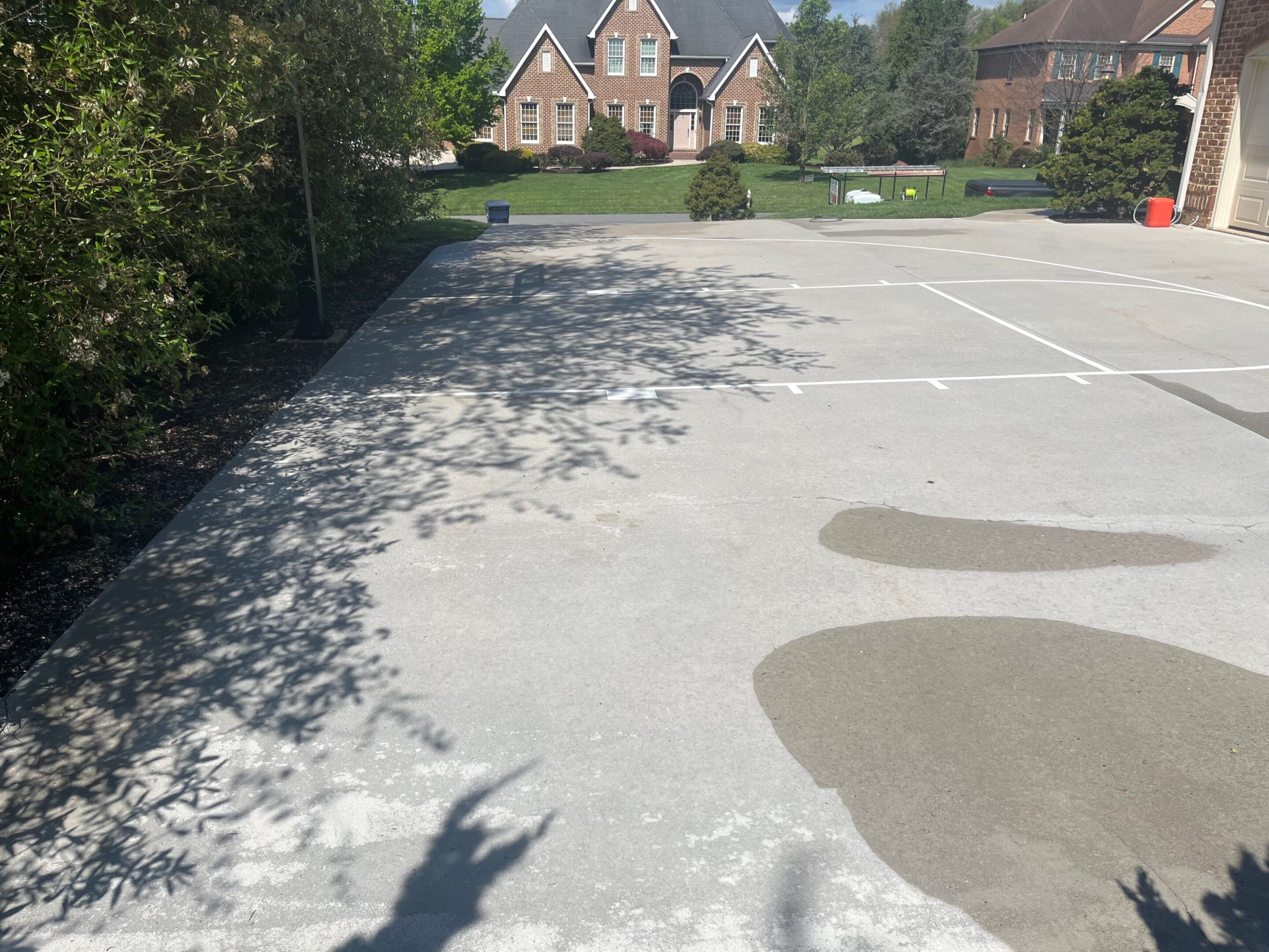 Empty parking lot with a large puddle and shadows of nearby trees.
