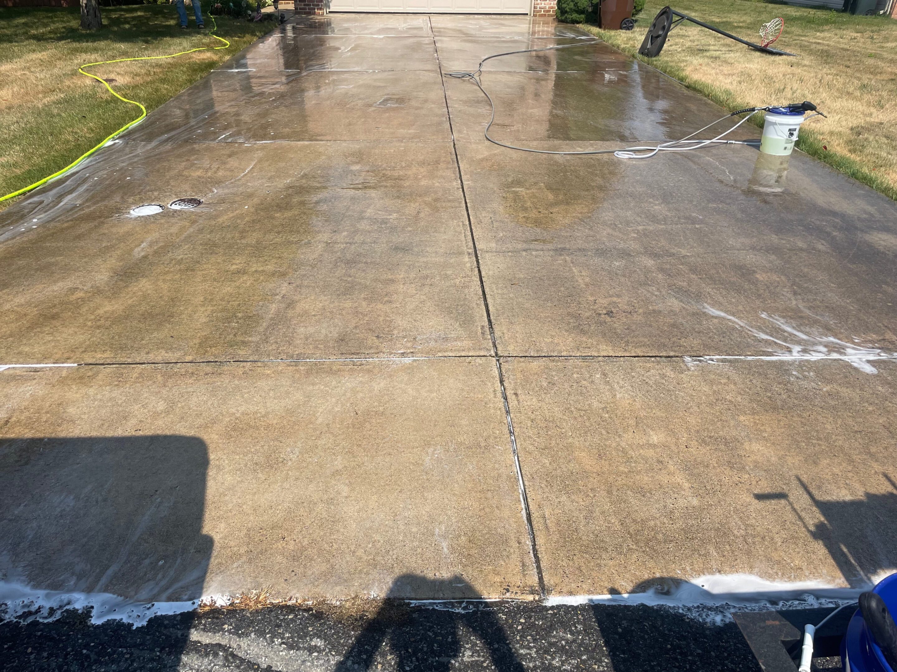Freshly cleaned concrete driveway with wet surface reflecting light.