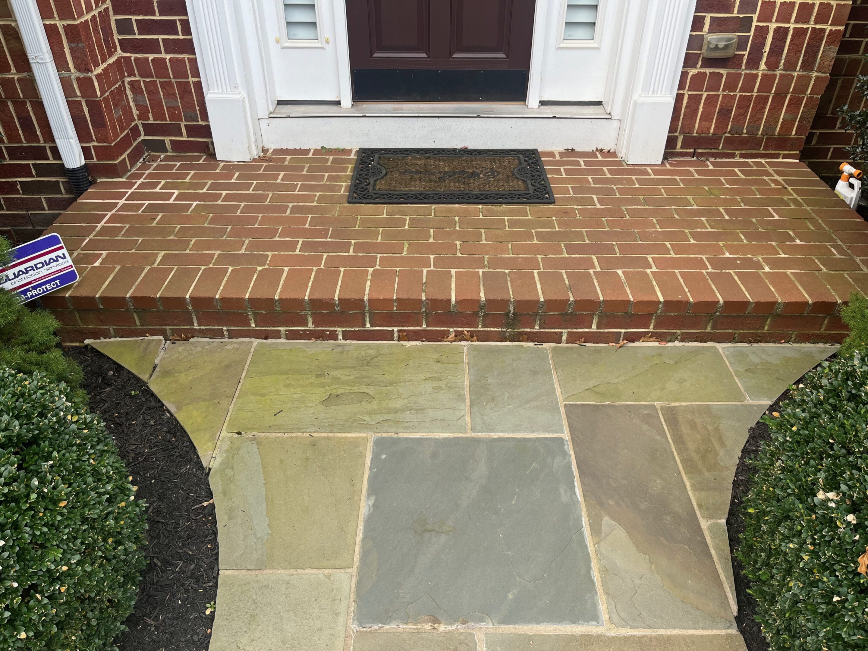 A brick porch with a doormat and a stone-paved walkway.