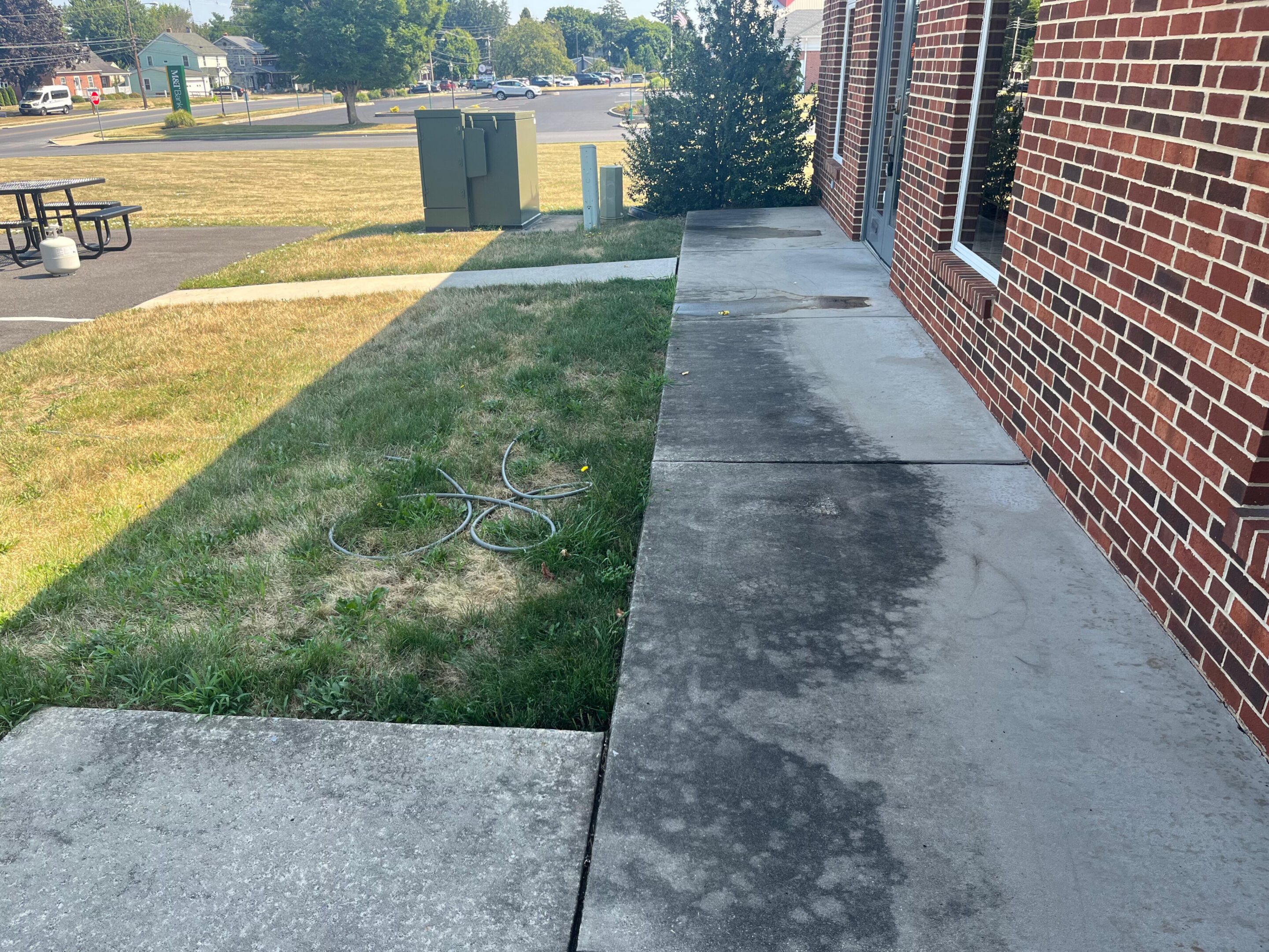 Sidewalk beside brick building with patchy grass and utility boxes in background.