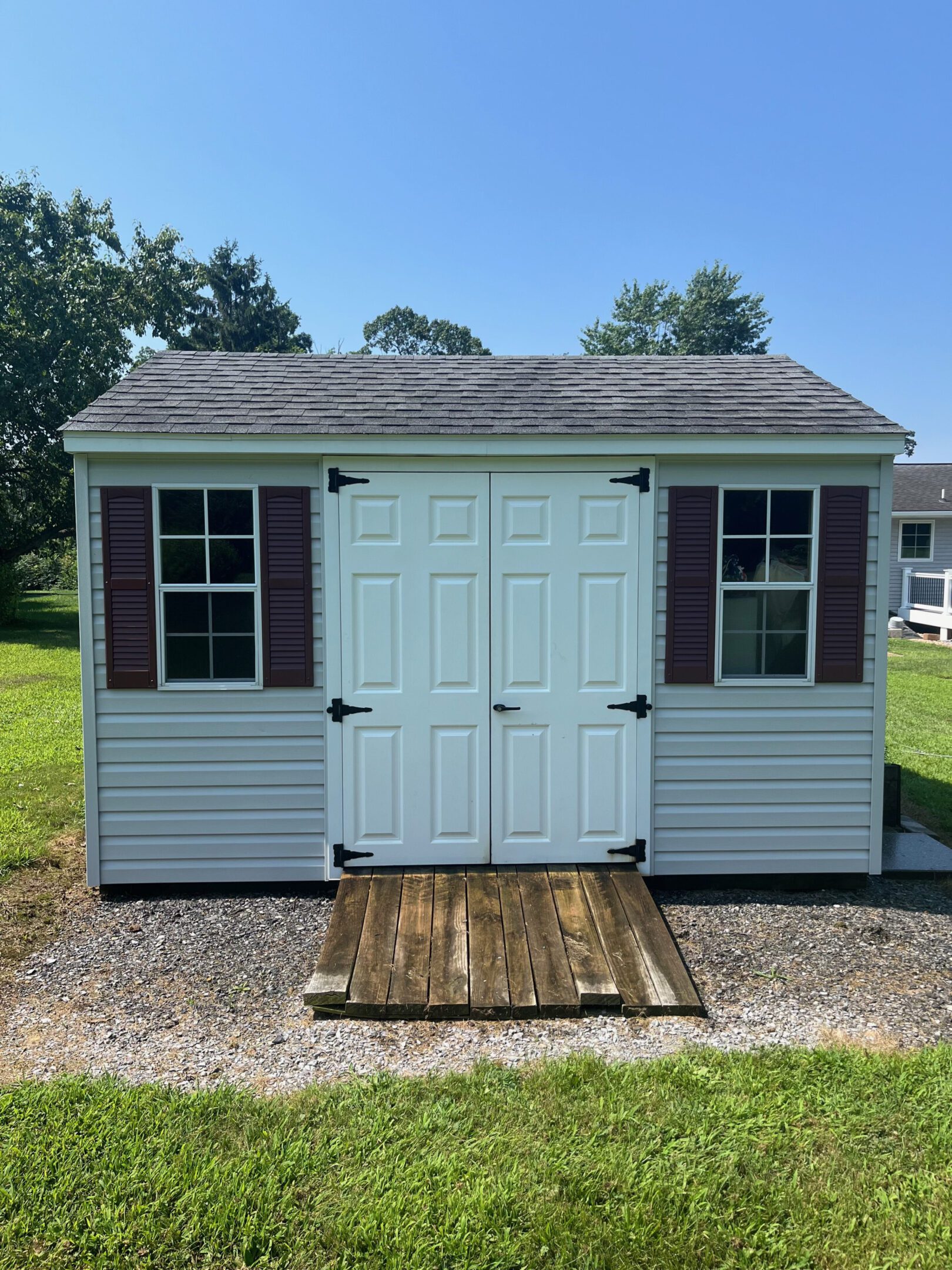 A small beige shed with double doors and two windows on either side.