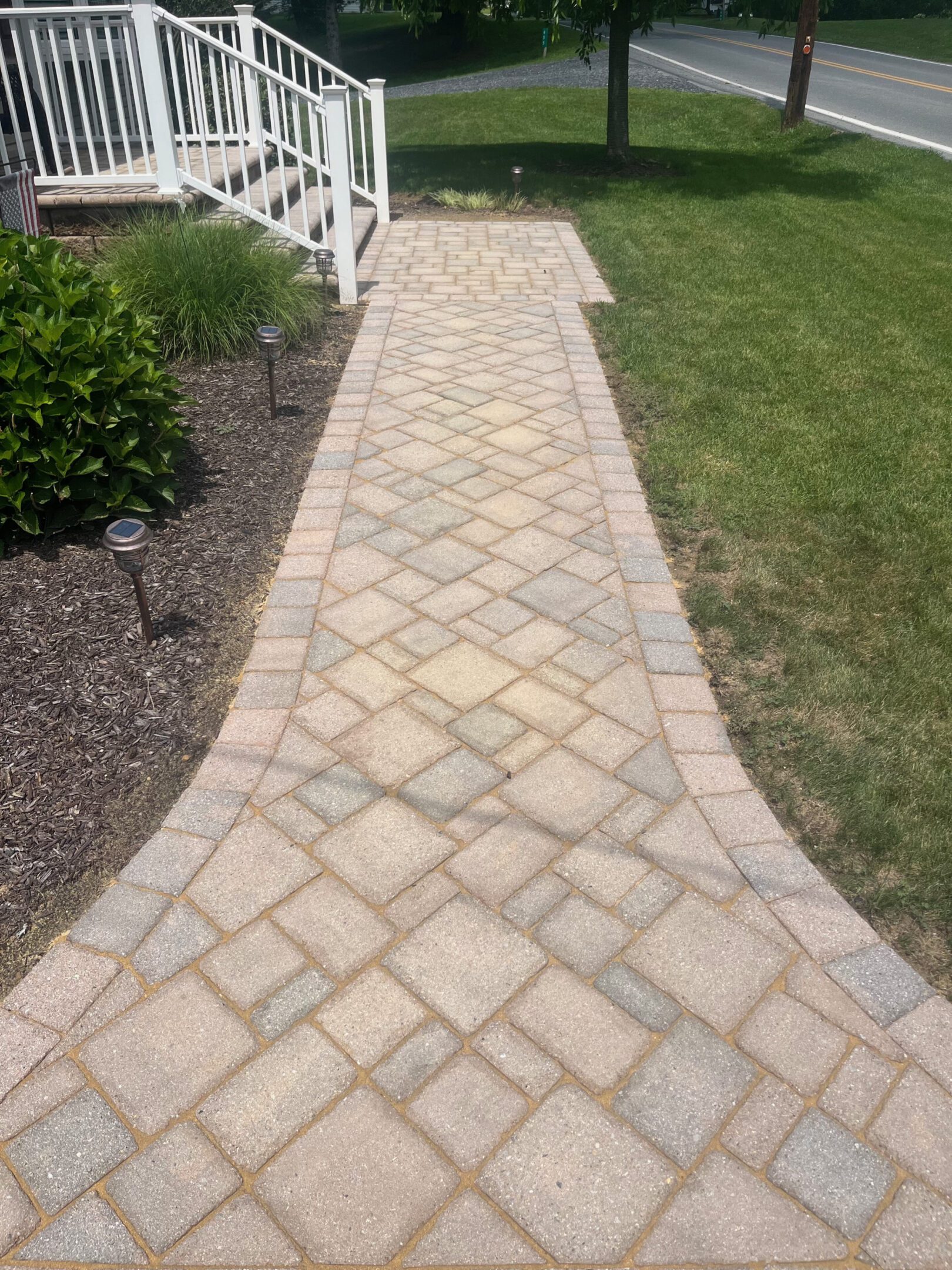 A paved stone walkway bordered by mulch and grass.