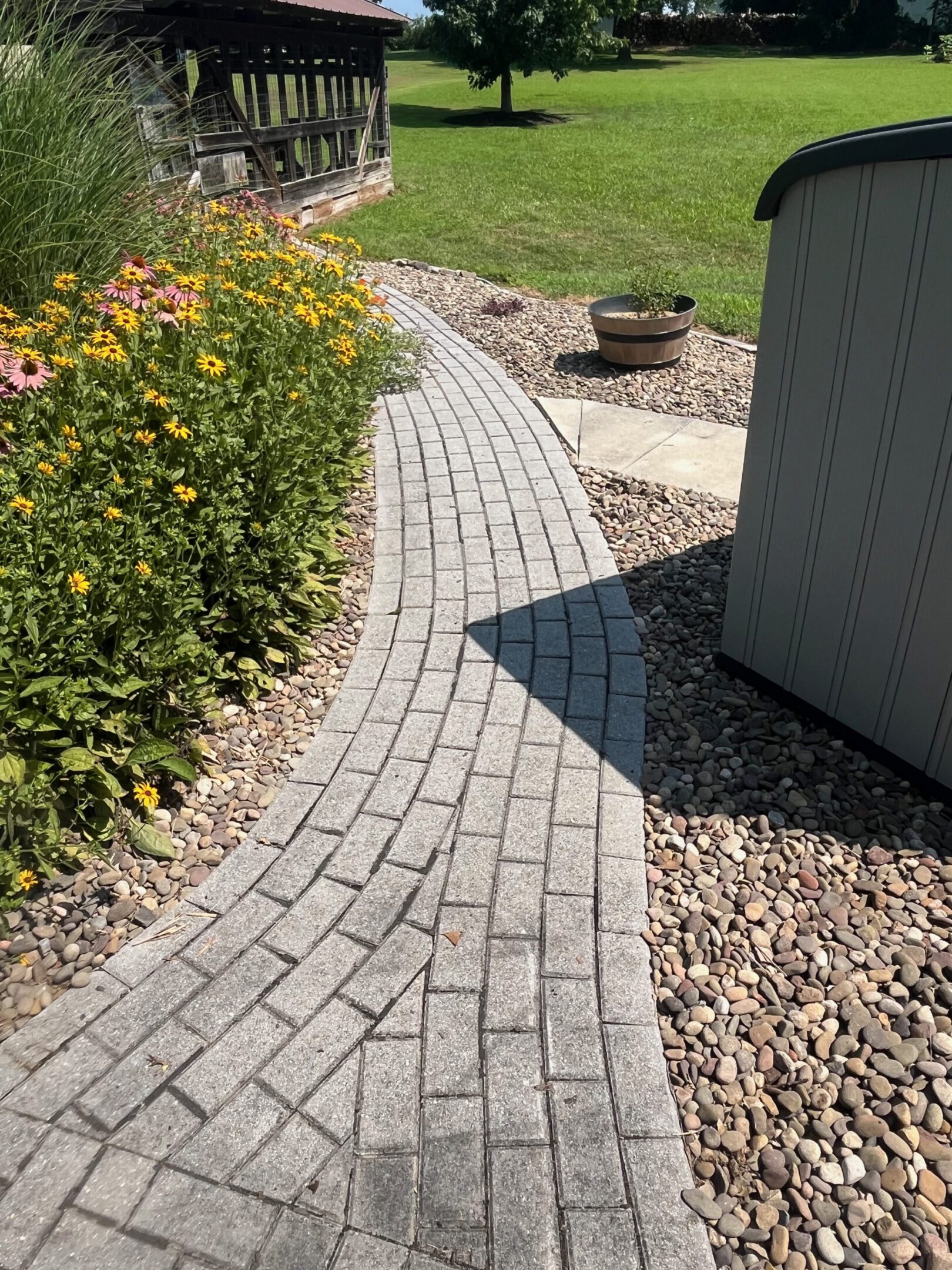 Curved brick pathway bordered by flowers and gravel leading to a fire pit.