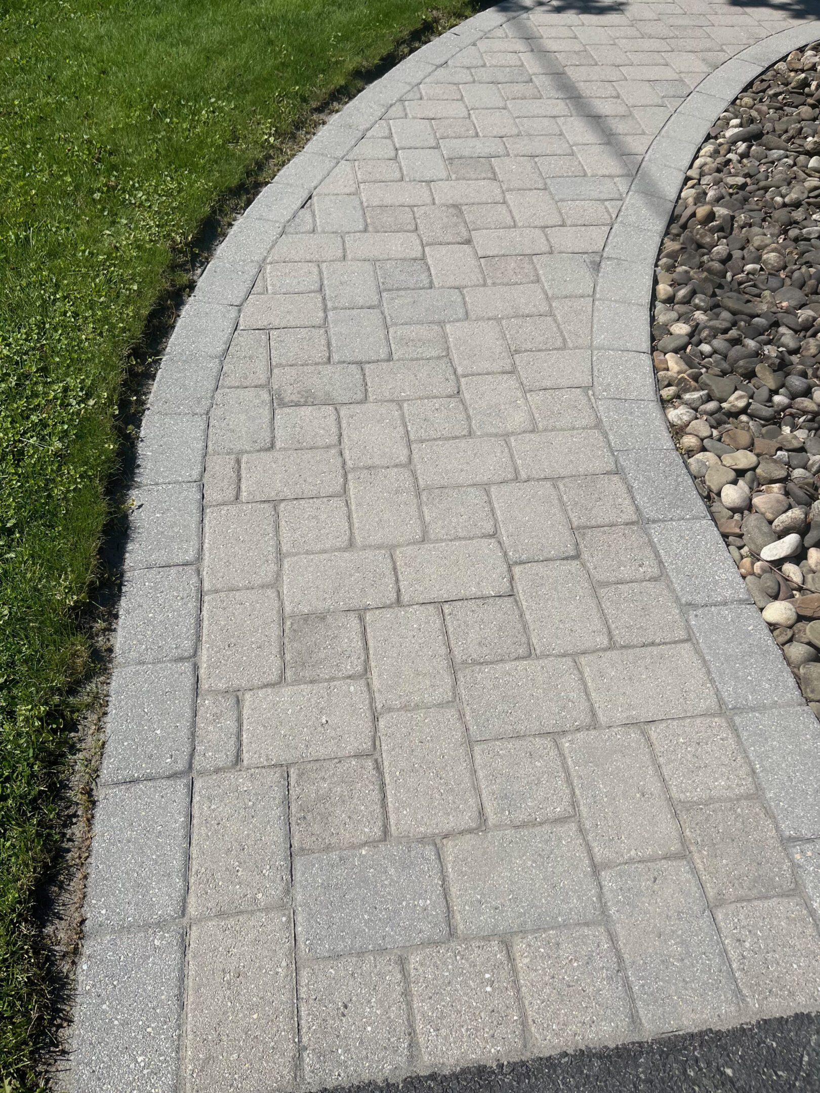 Clean gray paver path bordered by river rocks