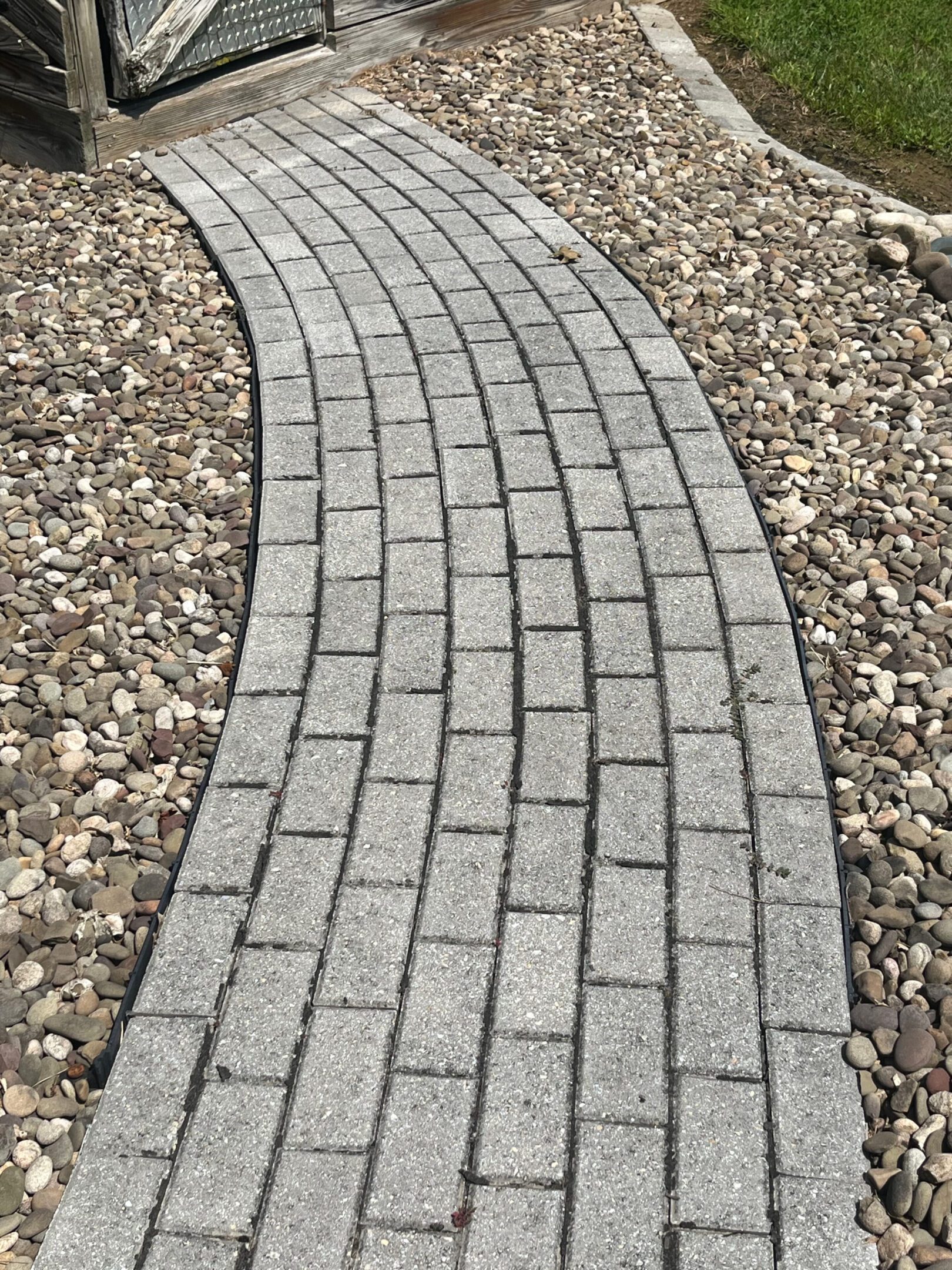 Curved pathway made of rectangular gray bricks surrounded by small rocks.