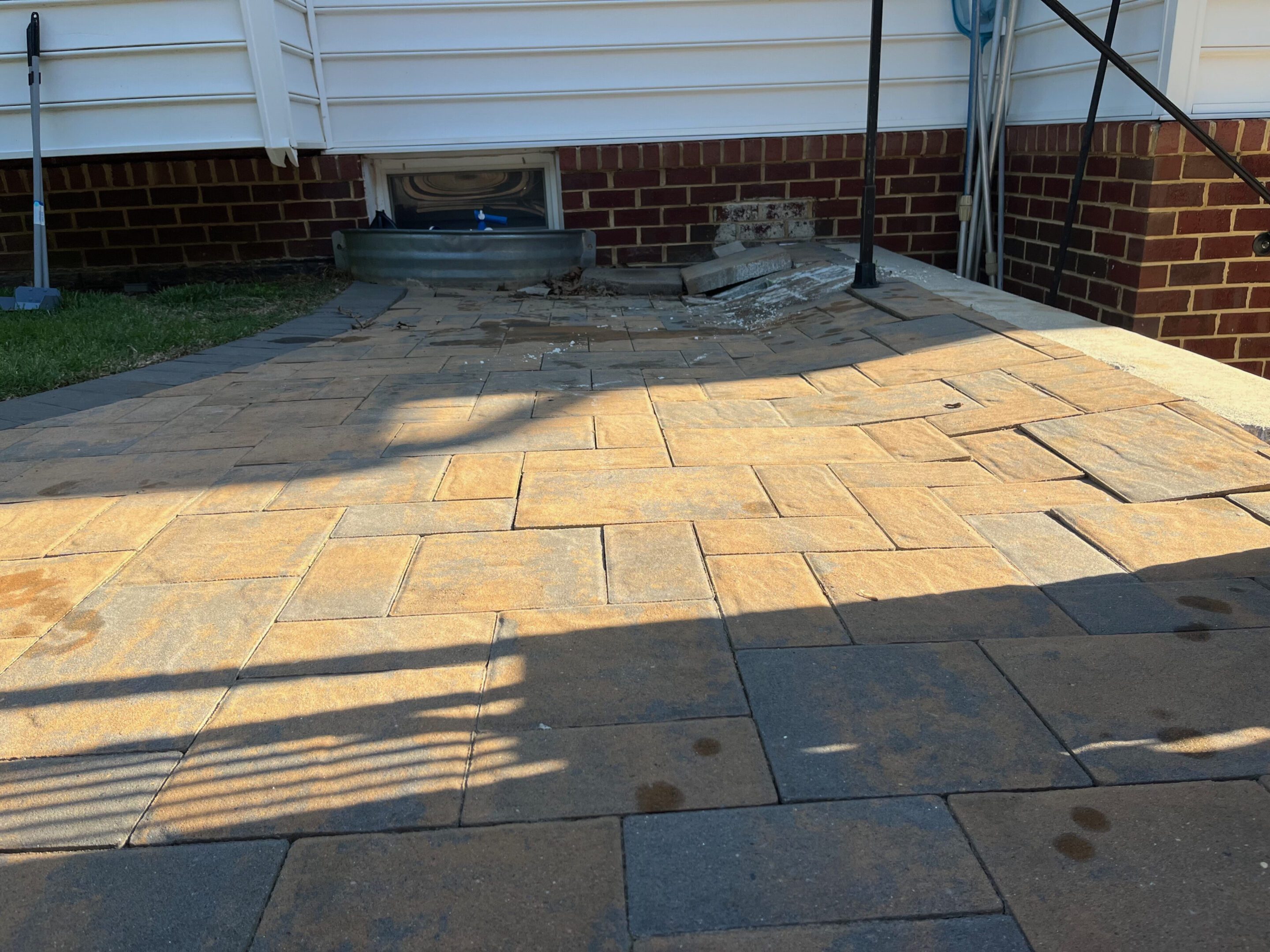 Sunlit stone patio with a white bench against a brick wall.
