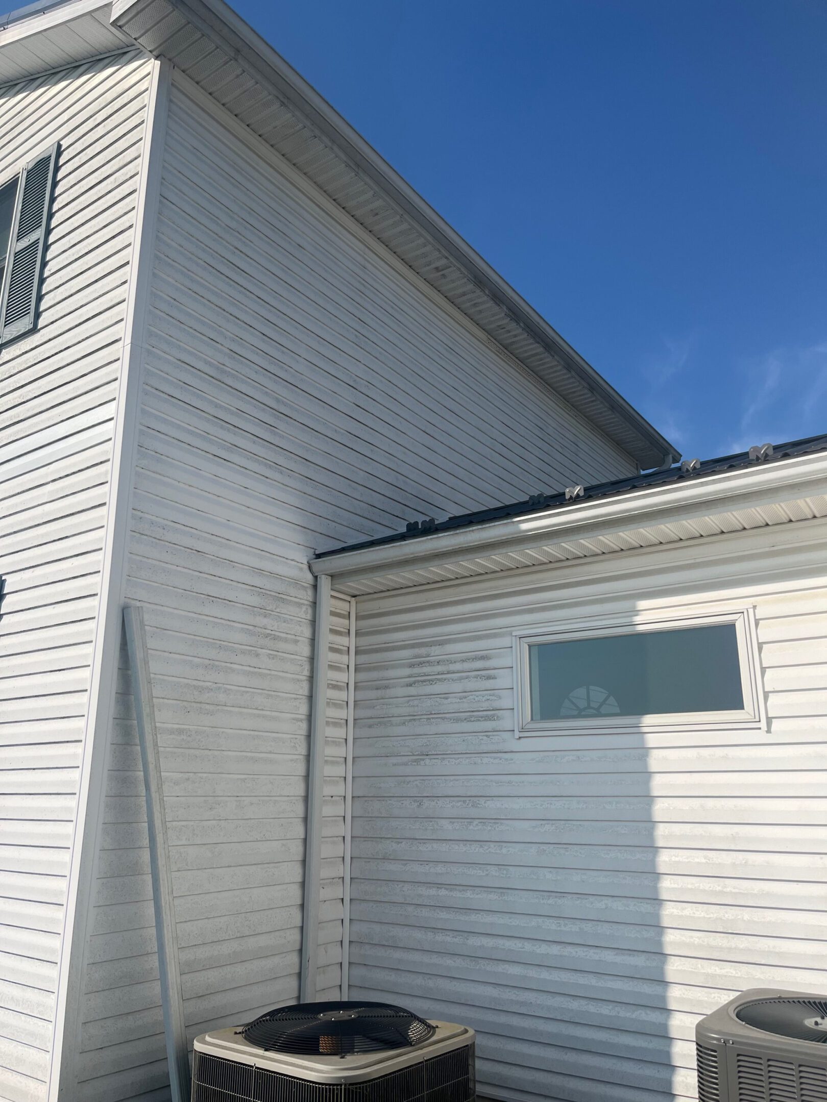 A white wooden house exterior with visible water stains and a small window under a blue sky.