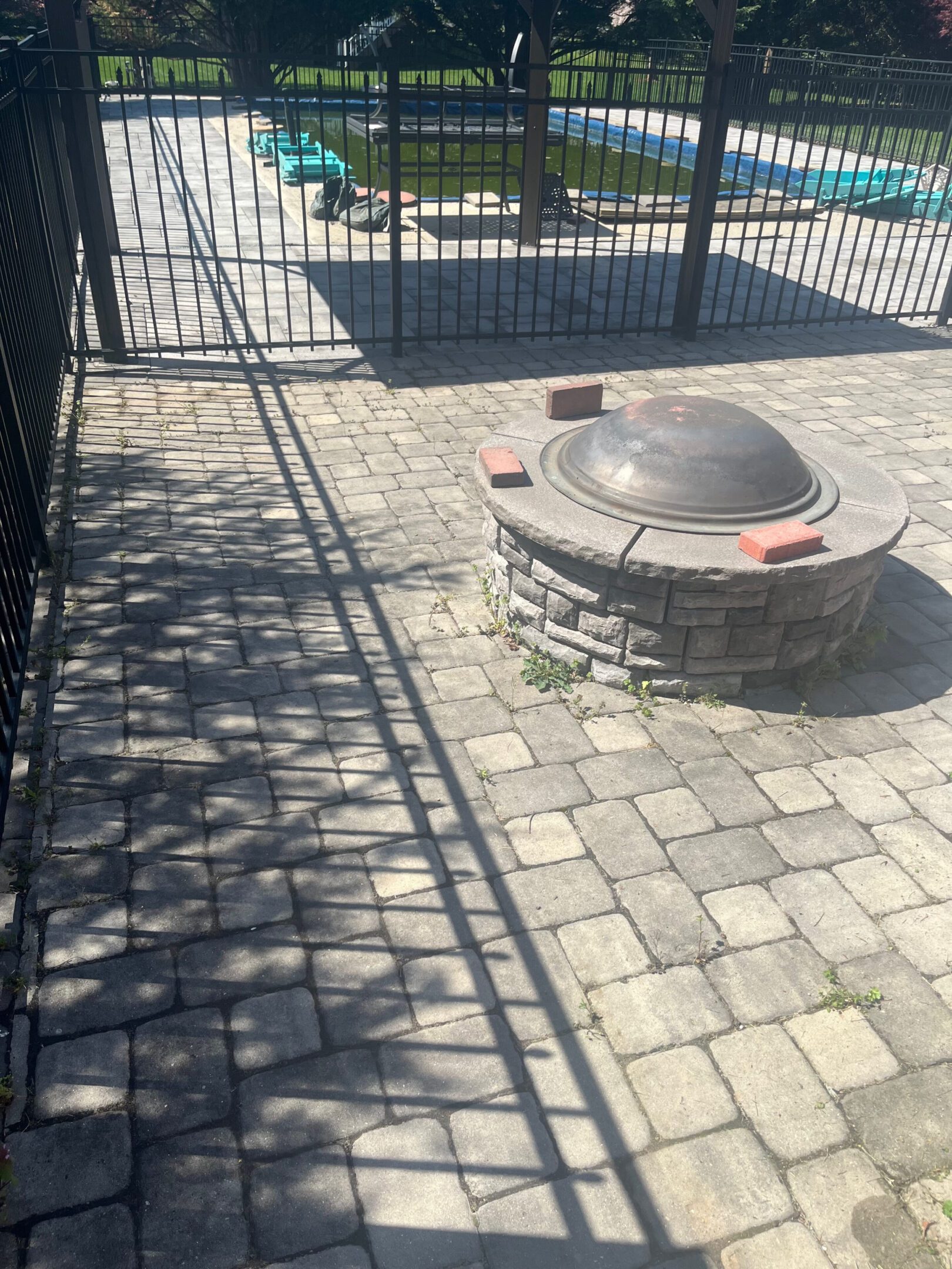 Outdoor fire pit on stone patio with shadows from fence and trees.