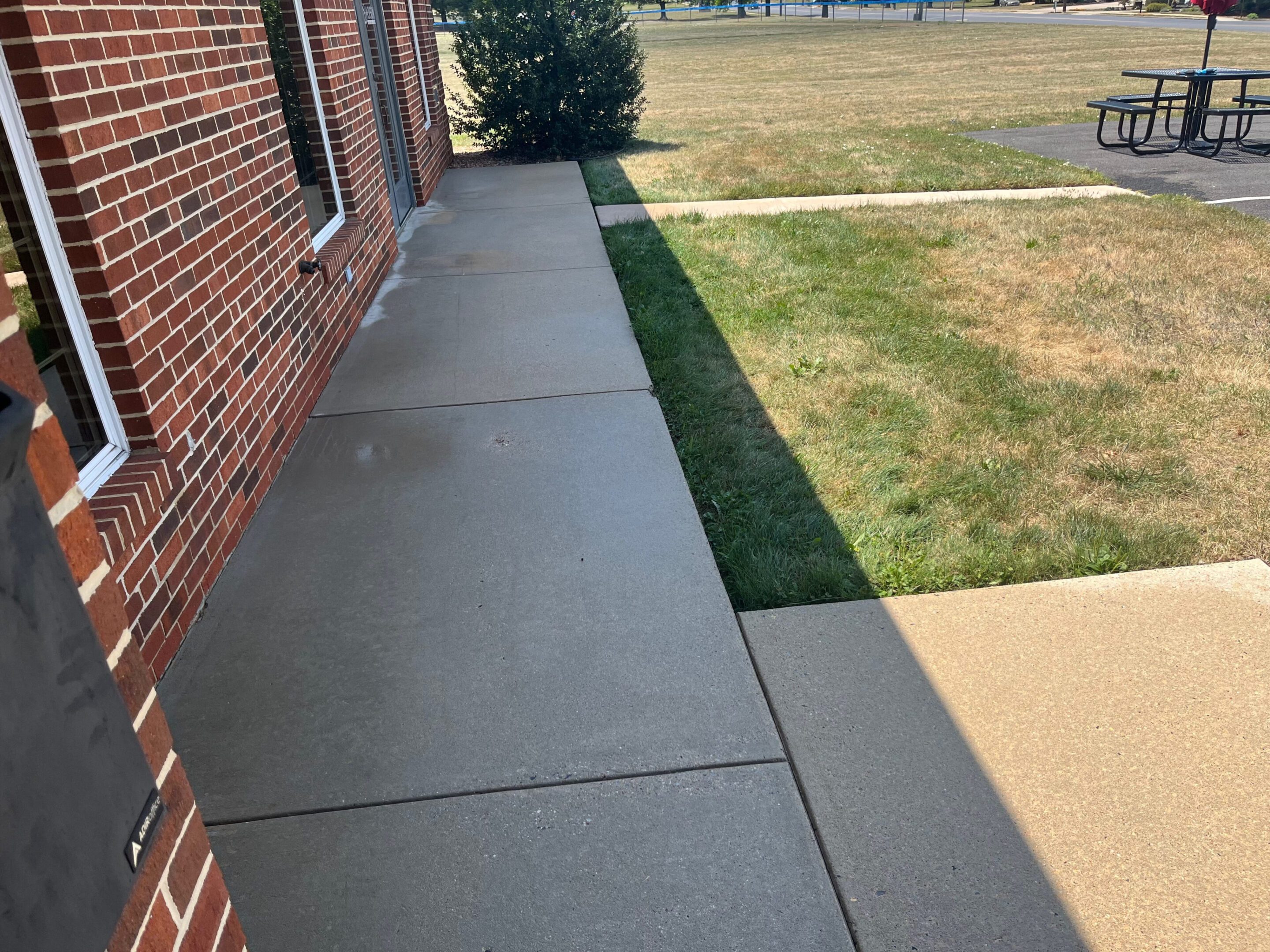 Freshly poured concrete sidewalk beside a brick building.