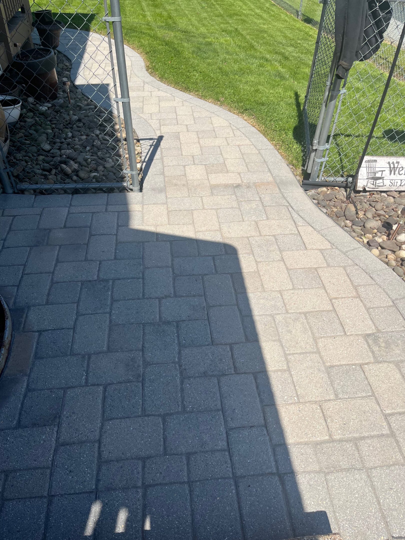 Sunlit stone pathway alongside a garden and house wall.