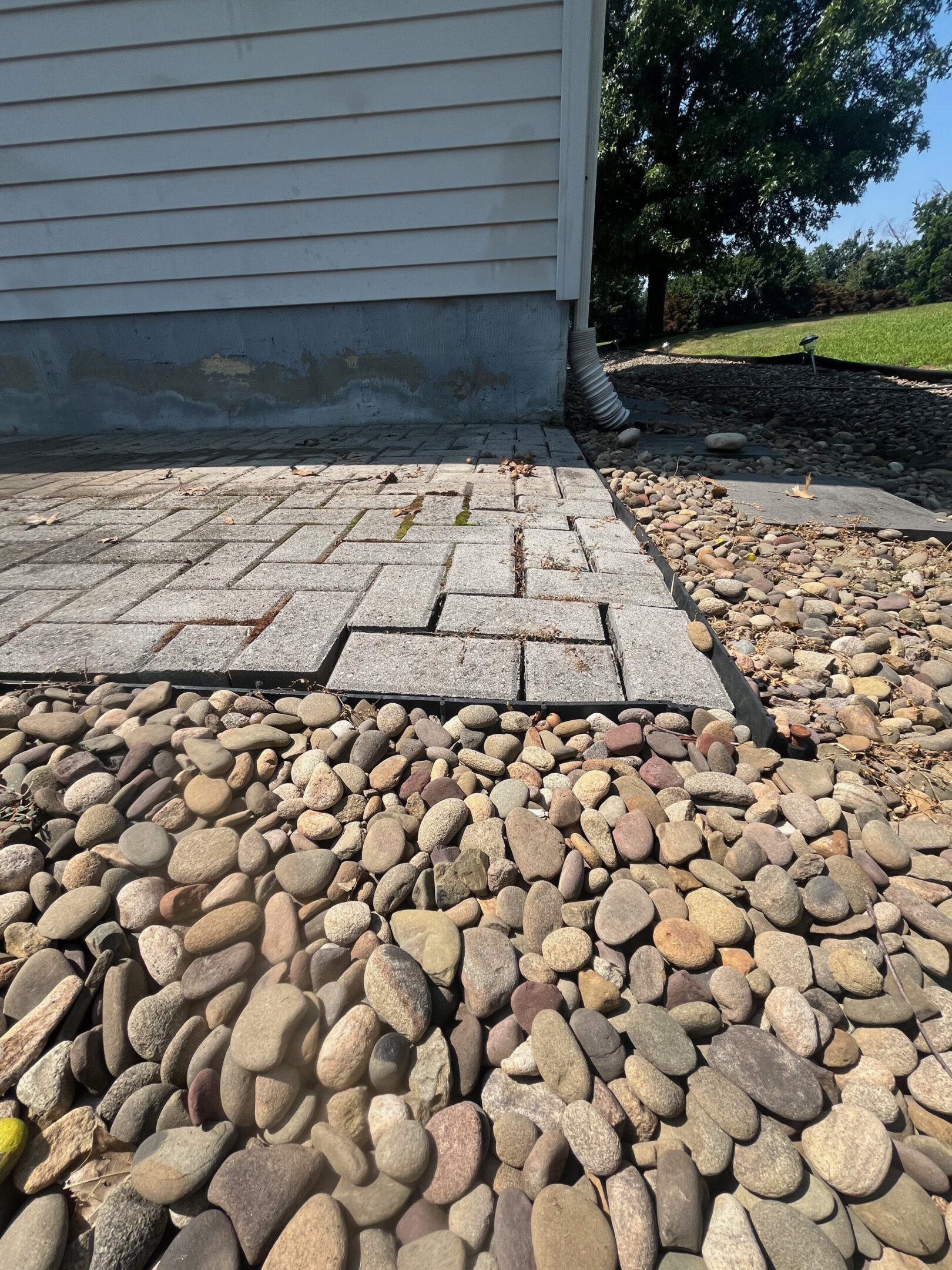 Close-up of a patio edge with interlocking pavers and river rocks.