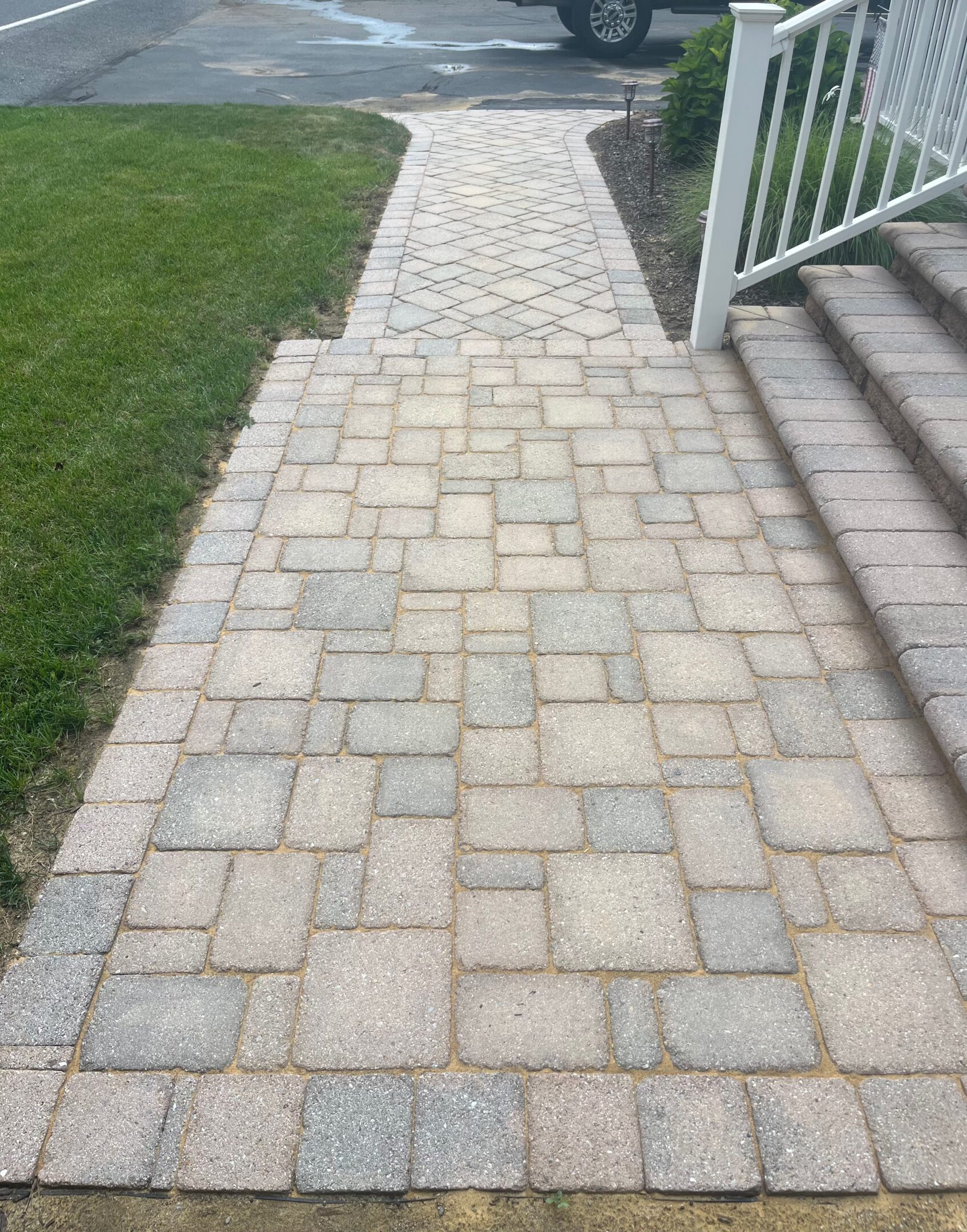 A paved stone walkway beside a grassy lawn and steps.