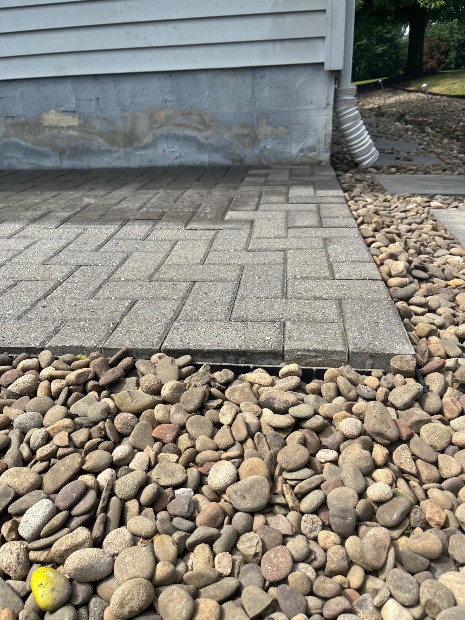 Concrete pavers transitioning to a bed of small rocks beside a building.