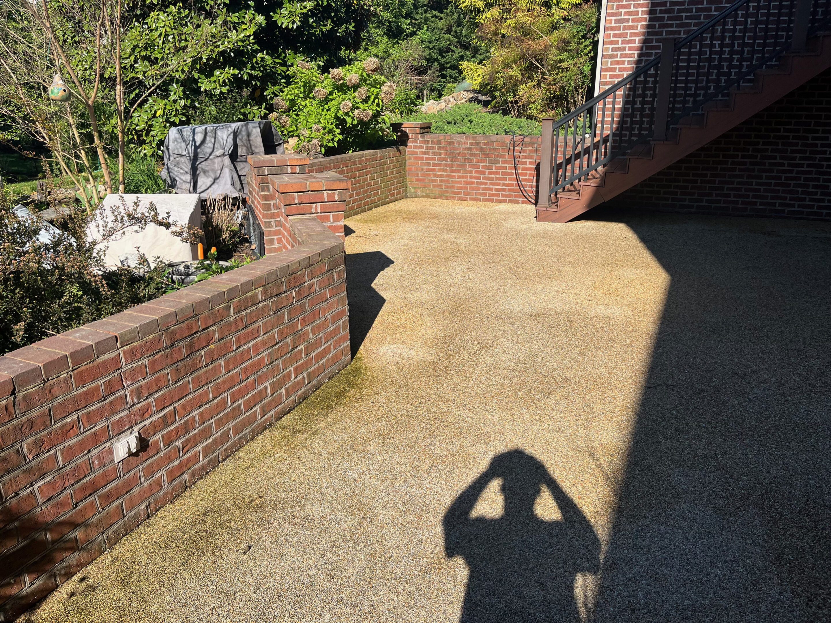 Sunlit pathway with brick walls and shadow of a person taking a photo.