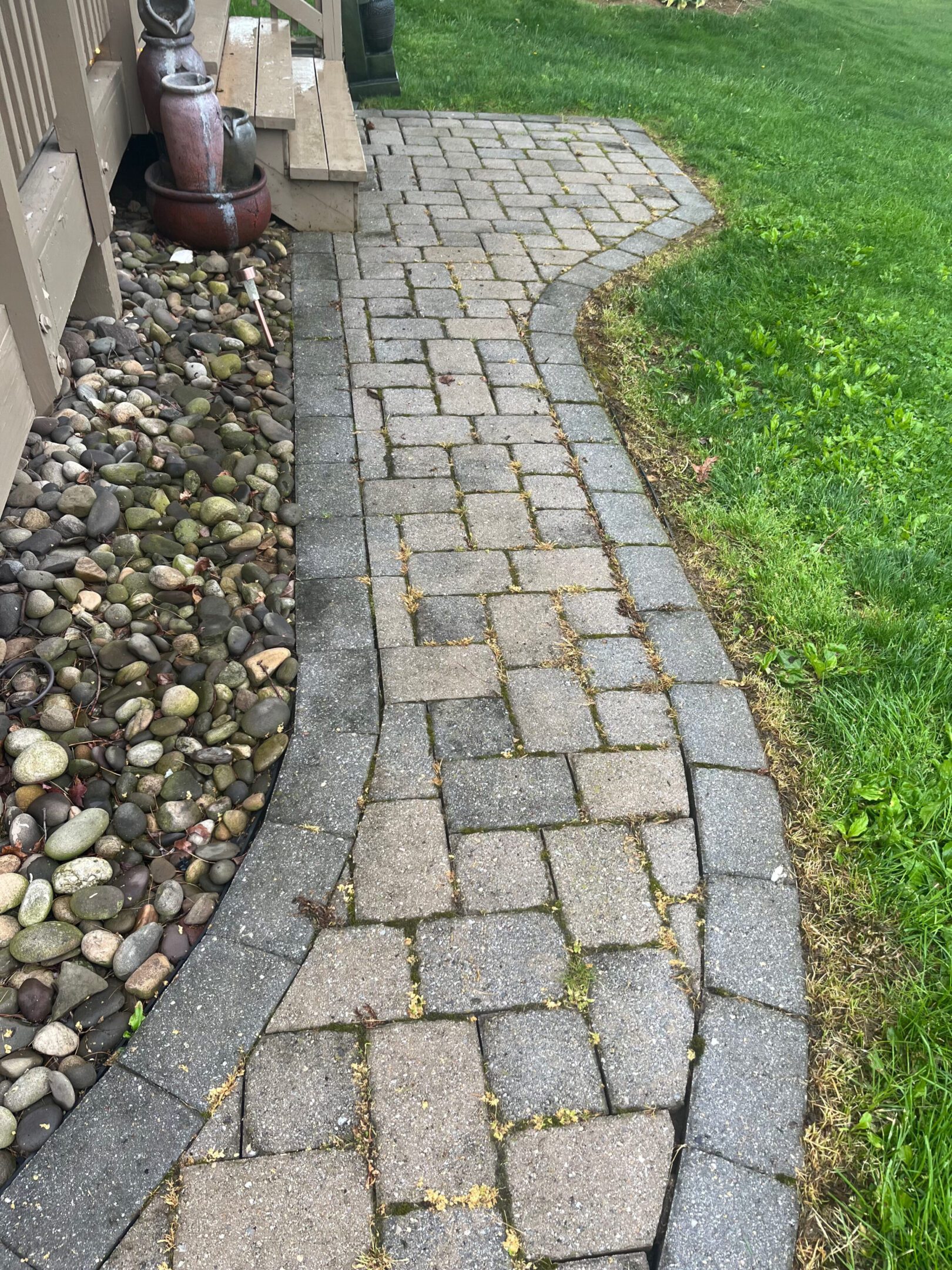 A cobblestone pathway curves beside a grassy lawn and a bed of river rocks.