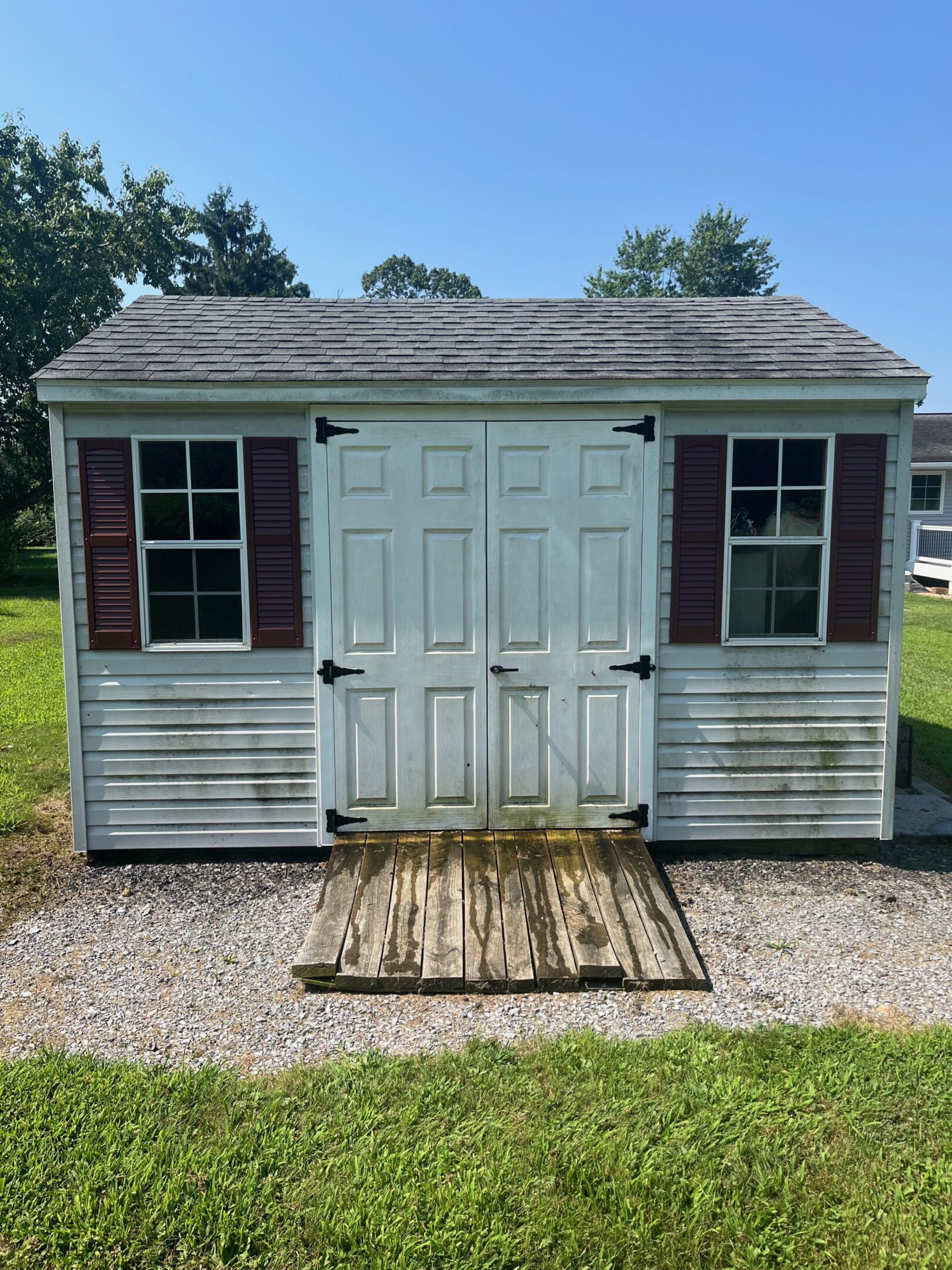 A weathered white shed with double doors and a ramp in front.